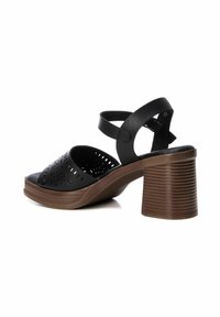 Scarpa nera open-toe con perforazioni a taglio, dotata di un tacco chunky marrone arrotondato e di una larga cinturini alla caviglia regolabile. Suola testurizzata.