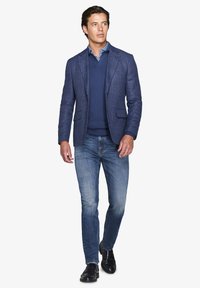 Marinefarvet ternet blazer, strikket marinefarvet sweater og lys blå skjorte med denimjeans. Sorte loafers fuldender outfittet. Renskåret, skræddersyet look.