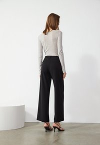 Haut à manches longues gris clair associé à un pantalon noir à jambes larges, présentant une texture lisse et un design minimaliste. Des sandales à talons noires complètent le look.
