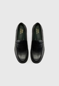 Zwarte leren loafers met een gladde afwerking, ronde neus, verhoogde stiksels en een groene binnenvoering; logo gedrukt in goud.