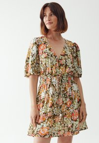 Floral dress featuring a deep V-neck, puff sleeves, and an elastic waist. Made of lightweight fabric with multicolored floral patterns on a brown base.