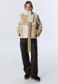 Beige en crème kleurblokjasje met gestructureerde fleece en een gebreide sjaal. Gecombineerd met zwarte neplederen broek en donkerbruine schoenen.