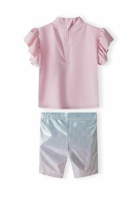 Haut rose à manches courtes avec des manches volantes et une fermeture éclair au dos ; shorts bleus brillants avec un motif en vagues.