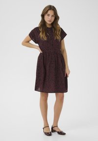 Robe florale bordeaux à manches courtes, avec un devant à boutons et une taille cintrée. Associée à des chaussures à bride de cheville bordeaux assorties.