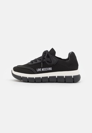 Czarny dziergany sneaker z białym napisem "LOVE MOSCHINO", czarnymi sznurowadłami i grubą, segmentowaną czarno-białą podeszwą na białym tle.