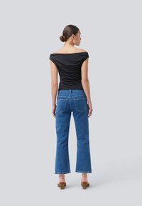 Zwarte off-the-shoulder top met een strakke pasvorm, gecombineerd met hoge, lichtblauwe flared jeans en bruine blokhak sandalen.