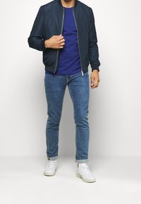 Námornícká bombarďák, modré tričko, světle modré džíny a bílé tenisky. Obsahuje zipové zapínání, žebrované manžety a srolovan�é džíny.