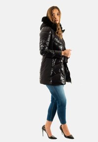 Giacca a vento nera, lucida e trapuntata, con cappuccio foderato in pelliccia, abbinata a jeans skinny blu e scarpe col tacco nere.