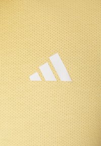 Tela amarilla texturizada con patrón de malla; presenta un gran logo blanco de tres rayas exhibido de manera prominente.