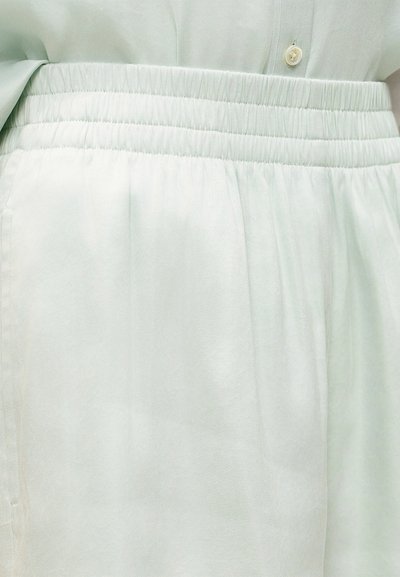 Gros plan de la ceinture élastique de couleur claire sur un pantalon en tissu doux, accompagné d'une chemise boutonnée assortie.