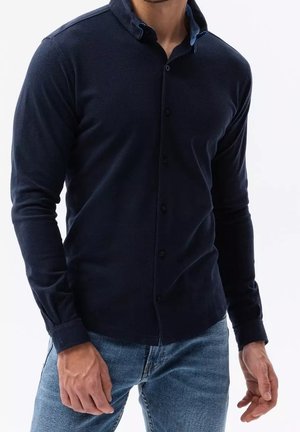 Chemise à manches longues navy avec une surface texturée, devant à boutons et accents de col bleu contrastants, associée à un jean en denim clair.