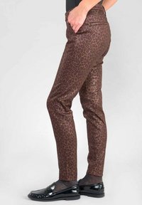 Pantalons à imprimé léopard marron avec une coupe slim, présentant une texture lisse et une taille mi-haute. Portés avec des mocassins noirs.