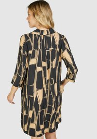 Schwarzes und beiges, gemustertes Kleid mit Kragen, Dreiviertelärmeln und lockerer Passform. Verfügt über eine Falte im Rücken.