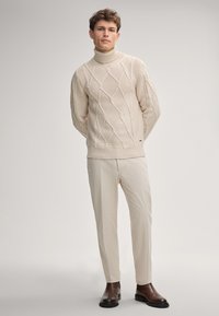 Beiger Rollkragenpullover mit diamantförmigem Muster, kombiniert mit hellen Hosen und braunen Lederstiefeln. Schlichtes und modernes Design.