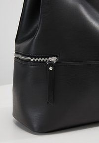 Coin de sac en cuir noir avec fermeture éclair argentée horizontale et languette en cuir noir sur un fond clair.