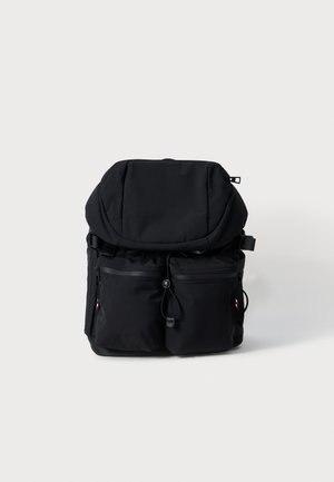 Black backpack with large top flap, two front zippered pockets, adjustable side straps, and a cord pull on front, shown against a plain background.
