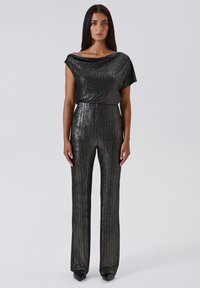 Jumpsuit nero scintillante con scollatura drappeggiata, gambe ampie e strisce verticali luccicanti, che mettono in mostra una silhouette elegante e aderente.
