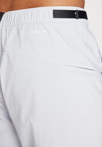 Lys grå shorts med en teksturert overflate og svart elastisk midjebånd. Har "FLASHDRY-XD"-logoen og diskrete sømmer på baksiden.