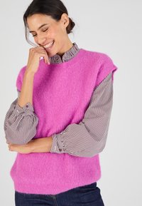 Roze gebreide trui met korte mouwen, met een losse pasvorm en zachte textuur, gedragen over een gestreept overhemd met knopen en opgeblazen mouwen.