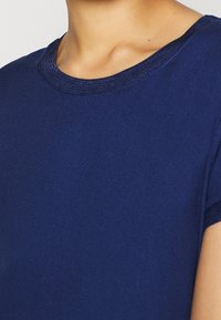 Maglietta blu navy con scollo rotondo. Tessuto liscio e morbido con una finitura a maglia testurizzata sul colletto e sulle maniche. Maniche corte.