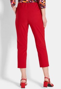 Rote, abgeschnittene Hosen mit einem dehnbaren Bund und glatter Textur, kombiniert mit roten Sandalen mit Blockabsatz. Der Stoff weist keine sichtbaren Muster auf.