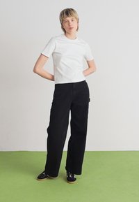 Hvid kortærmet t-shirt, sorte vide bukser og sorte sneakers. Enkel design, ensartet tekstur og ingen synlige mønstre eller akcenter.