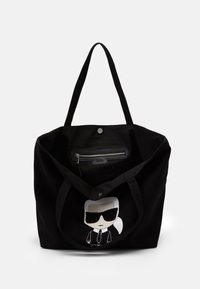 Černá taška s dlouhými uchy, otevřeným vrchem, vnitřní zipovou kapsou a potiskem karikaturní postavy v slunečních brýlích a obleku na přední straně.