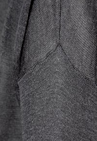 Mörkgrå stickad tröja med ett texturerat mönster, ribbade detaljer på axlarna och en sömlös halsdesign. Mjuk tyg med lätt lyster.