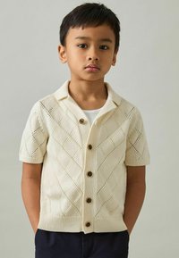 Kurzarm-Strickjacke in Creme mit Rautenmustern, Knopfverschluss und einem Kragen-Design. Die Textur ist weich und atmungsaktiv.