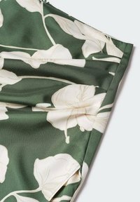 Tissu vert avec un grand imprimé floral blanc et des coutures visibles, plié sur les bords sur un fond clair.