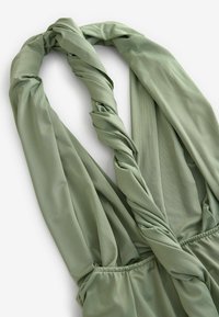 Grüner, leichter Stoff mit verdrehten Trägern und elastischer Raffung an der Taille, der eine glatte Textur und subtilen Glanz aufweist.