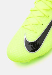 Fotbalová kopačka Nike v jasně neonově žluté barvě s texturovaným svrškem, černým logem Swoosh a tenkými, plochými šňůrkami. Průhledná podešev s kolíky pro lepší přilnavost.