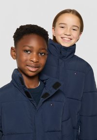 Marina pufferjackor med hög krage, som har kardborreaccents och horisontell sömnad. Två modeller, en med kort hår och en med medellångt hår.