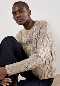 Maglione beige a maglia cable con dettagli in filo metallico, con scollatura a girocollo e maniche lunghe, abbinato a jeans blu scuro.