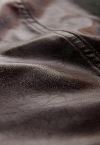 Gros plan sur un tissu en cuir marron foncé avec des plis visibles et un détail de couture cousue.