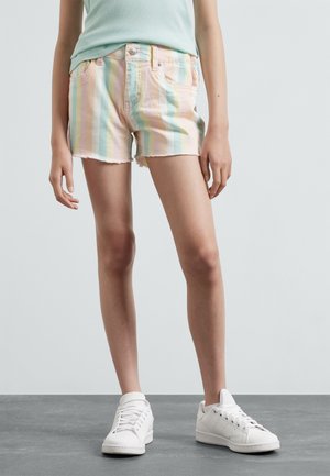 Pantalones cortos de mezclilla a rayas en colores pastel, con dobladillo deshilachado y dos bolsillos delanteros. Combinados con zapatillas blancas y una camiseta de color verde azulado claro.