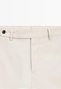 Beige katoenen broek met een fijne textuur, voorzien van een zwarte knoop, ceintuurlussen en een frontale plooi. Eenvoudig, op maat gemaakte vormgeving.