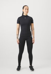 Top sportivo nero a maniche corte con leggins aderenti. Tessuto liscio, design aderente, con un logo sottile sul petto e sulla vita.