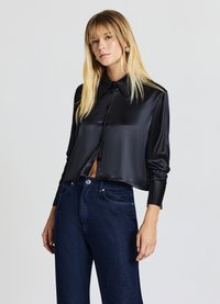 Schwarzes Satinhemd mit einer Knopfleiste vorne, einem Kragen mit strukturiertem Design und langen Ärmeln mit gerippten Bündchen, kombiniert mit dunklen Denim-Jeans, die mit Nieten verziert sind.