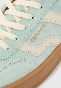 Világoskék velúr sportcipő krémszínű fűzőkkel, bézs bőr részletekkel, barna gumitalppal, és oldalt hímzett "GANT" logóval.