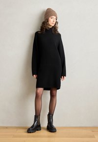 Černé žebrované pletené šaty s vysokým výstřihem a dlouhými rukávy. Kombinované s černými kotníkovými botami s leopardím vzorem. Světlohnědá pletená čepice.