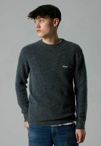 Mörkgrå ribbad tröja med rund halsringning och långa ärmar. Har en liten broderad logotyp på bröstet. Matchas med blå jeans.