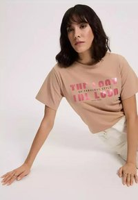 Beżowy t-shirt bawełniany z krótkim rękawem, z dużym różowym napisem "WYGLĄD WSPANIAŁEGO STYLU" oraz "CROSS JEANS" na środku.