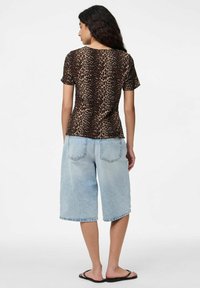 Leopardmönstrad topp med kort ärm, tillverkad av sl�ät tyg. Bärs med ljusblå denim Bermuda-shorts och svarta flip-flops; neutral bakgrund.