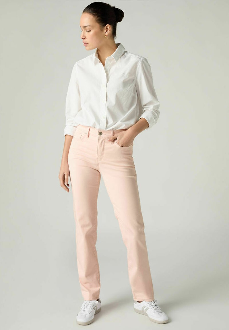 Jean rose clair avec un design ajusté, style cinq poches et fermeture par bouton, associé à une chemise blanche boutonnée et des baskets blanches.