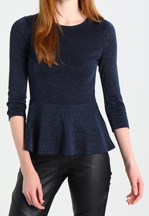 Granatowa bluzka peplum z rękawami do połowy łokcia; wykonana z fakturowanego, błyszczącego materiału. W zestawie z czarnymi dopasowanymi skórzanymi spodniami.