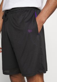 Black mesh athletic shorts with purple accents and logo, featuring an elastic waistband and side pockets. Textured fabric for breathability.