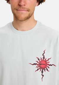 Light gray cotton t-shirt featuring a red sun graphic with wavy rays. Standard crew neckline and short sleeves, soft texture.