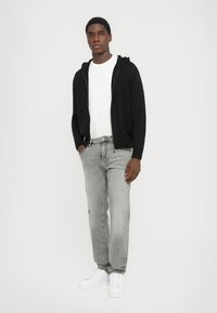 Sort zip-up hoodie, hvid t-shirt med rund hals, grå jeans og hvide sneakers. Outfittet har en afslappet pasform med et casual look.