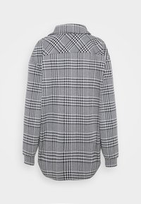 Chemise à manches longues à carreaux pied-de-poule noir et blanc avec col, vue de dos sur fond blanc.